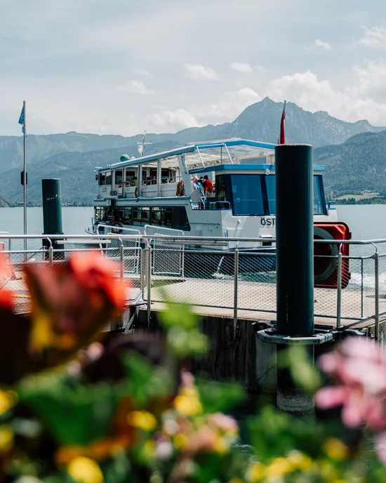 Barca turistica attraccata al molo sul Lago Wolfgang con montagne sullo sfondo e fiori in primo piano